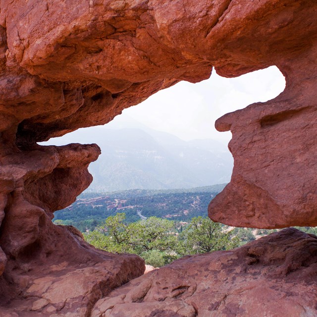 a view of a vegetated landscape through a red rock arch