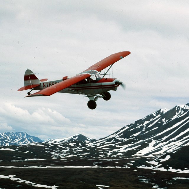 a red and white plane flies above mountains during spring