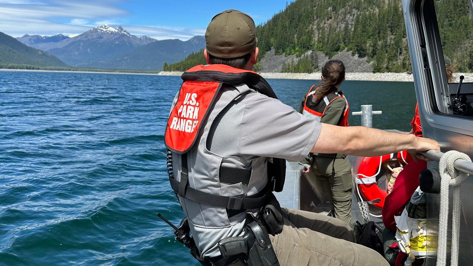 Park Ranger sitting on the side of the boat looking towards the lake and mountain in the distance