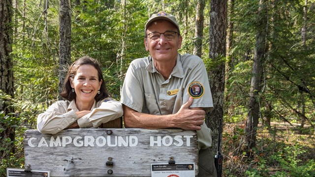 two people smiling in front of a camp host sign. 
