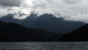 Clouds cover mountaintops on the far side of a lake.