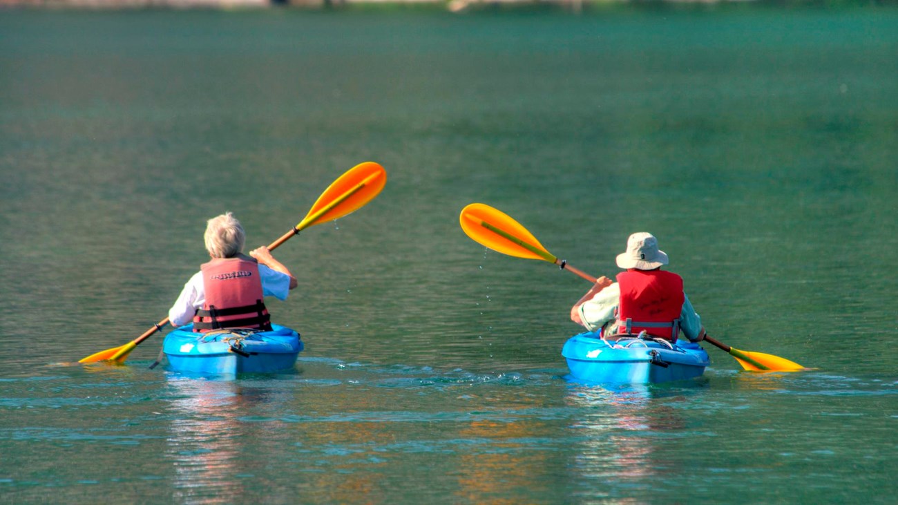 Two kayakers paddle on a lake.