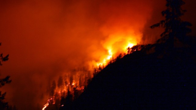A wildfire burns behind a silhouetted mountain.