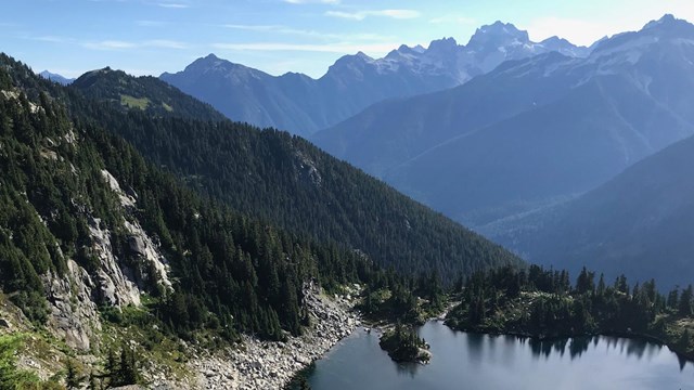 A small subalpine lake with a sea of mountains in the background.