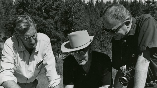 A historic photo of three men pointing a map on a table 