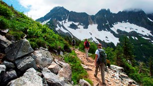 Three hikers travel along a dirt trail in the mountains.