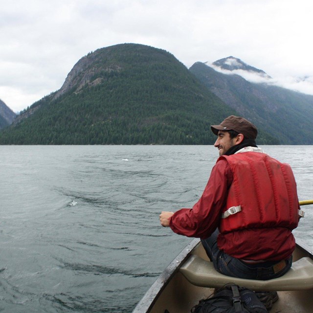 A person in a canoe floats on a lake surrounded by mountains.