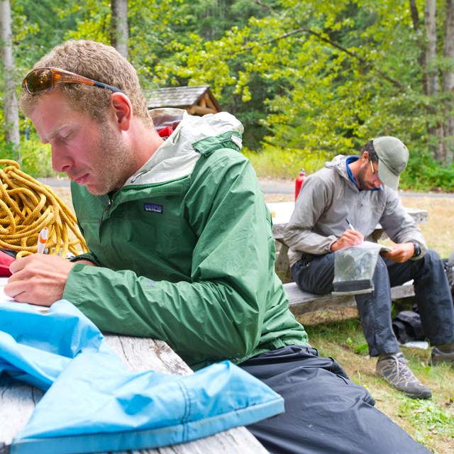 Two mean sitting on a picnic bench while reading in the Colonial Creek South Campground.