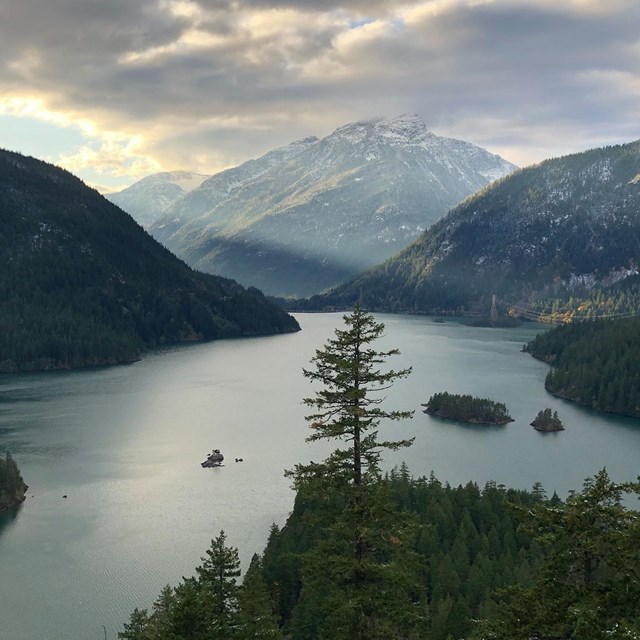 A blue lake surrounded by forested, snowy mountains.