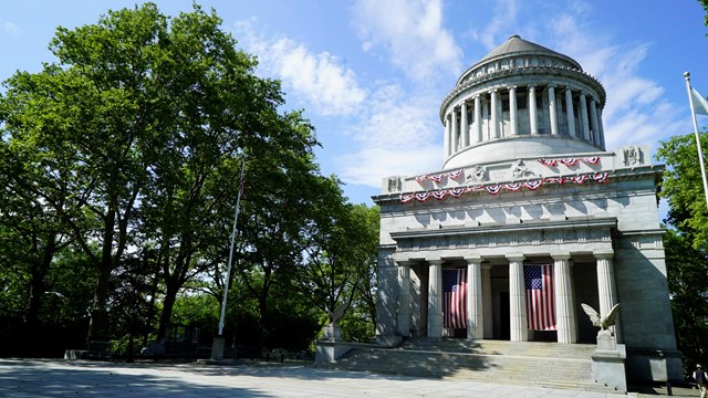 A marble mausoleum with a large dome stands tall against a bright blue sky 