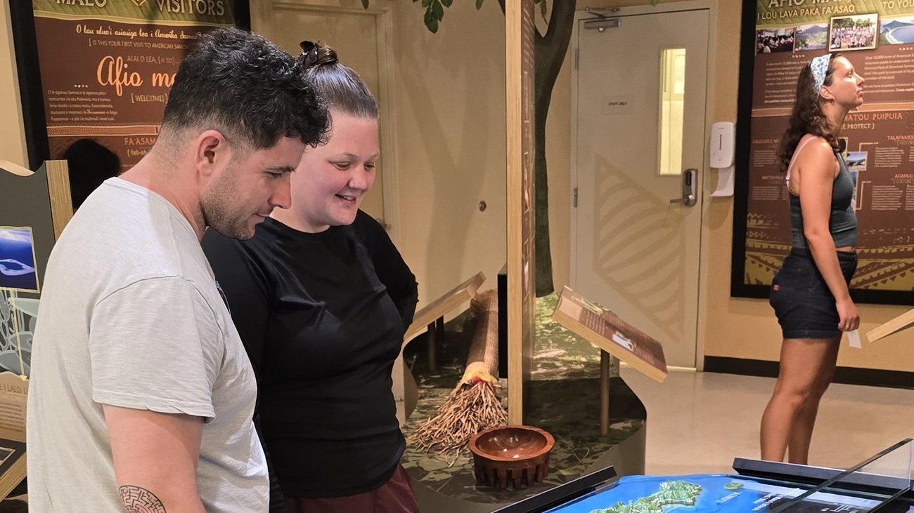 Indoors; two adults looking at a map with another person in background looking up at exhibit.