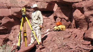 Scientists with a surveying tripod and cases along a canyon wall