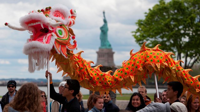 Statue of Liberty National Monument in the distance as in the foreground, a Chinese dragon puppet is held aloft.