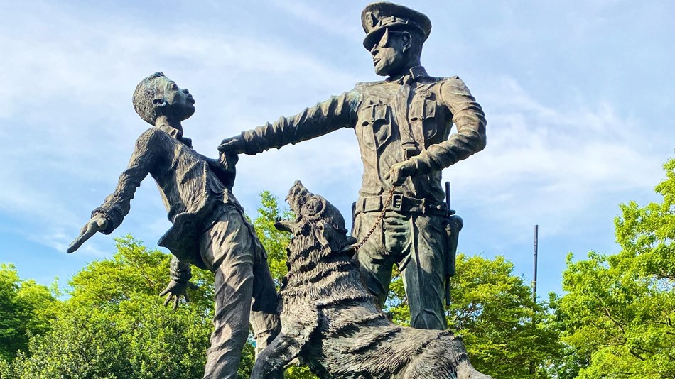Statue of a child being grabbed by a police officer with an aggressive dog