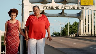 Two visitors holding hands next to the Edmund Pettus Bridge