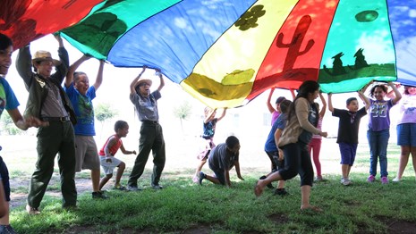 People holding up a giant parachute as a person runs underneath