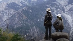 Two women trail crew workers looking over a mountainous valley
