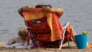 Dog laying next to a person in a chair on a beach