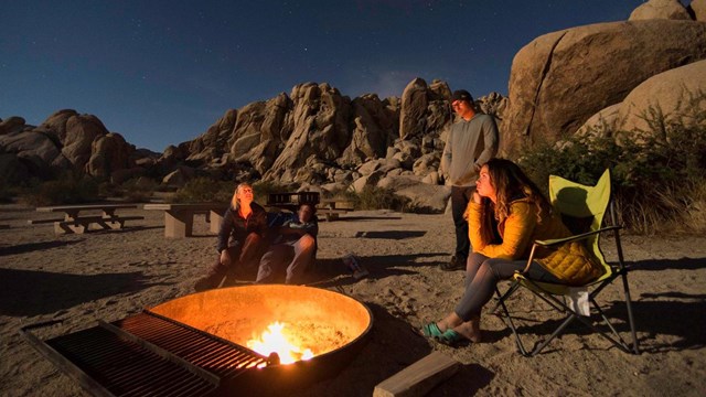 Campers sitting in chairs around a campfire under the night sky
