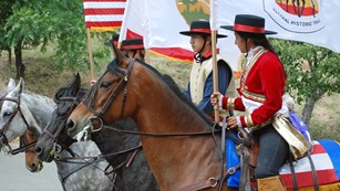 Three horse riders carrying a US, National Park Service, and trail flag
