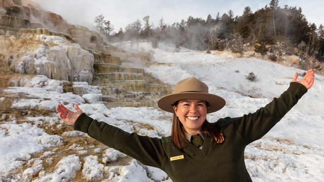 Smiling ranger holding up arms while standing outside in the snow