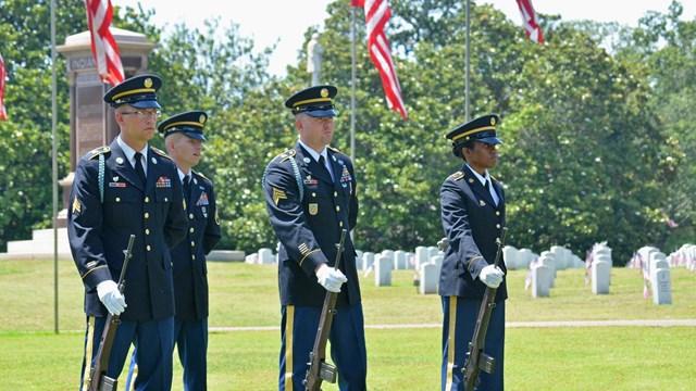 Soldiers in a color guard standing in a cemetery