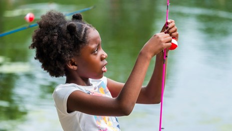 Child tying a fishing line to a rod
