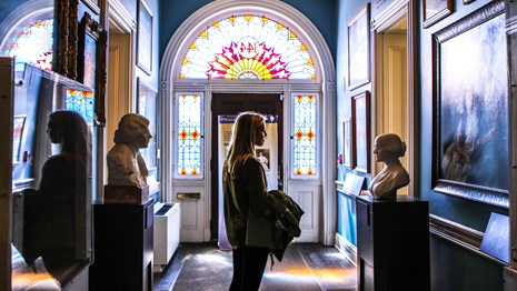 Visitor looking busts and paintings of suffragists in a hallway