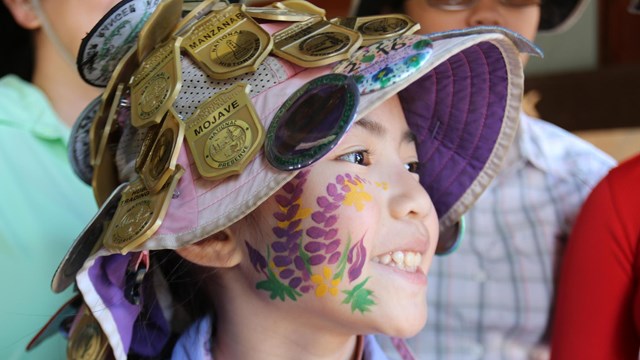 Girl with flower face-paintings and a hat covered with Junior Ranger badges