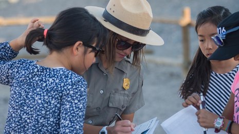 Ranger helping three kids writing in Junior Ranger books