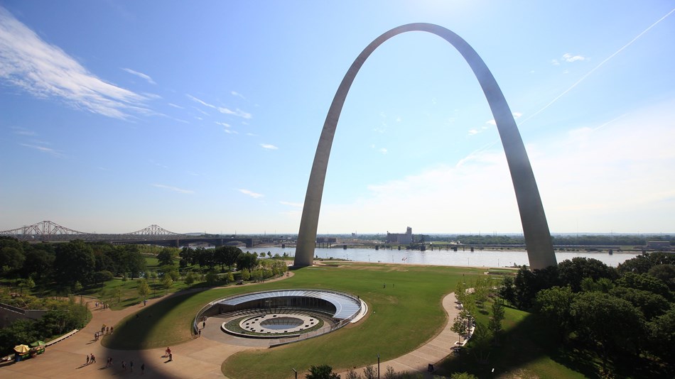 Overview of a giant metal arch structure in a city park next to a river