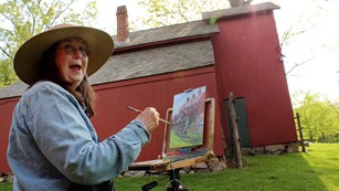 Painter painting a red barn on the other side of her canvas