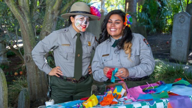 Two rangers creating paper flower decorations and one wearing Dia de Muertos facepaint  