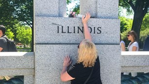 Person putting small bouquet of flowers on top of a memorial for Illinois