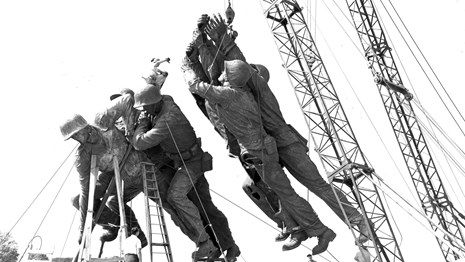 Historical black and white photo of statues of Marines lifted by a crane during construction