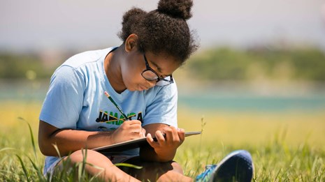 Visitor writing in a journal sitting in a field