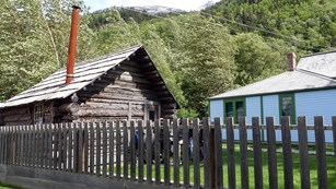 Wooden cabin and white house behind a picket fence