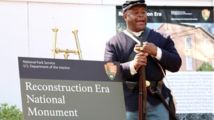 19th-century military reenactor next to a sign for Reconstruction Era National Monument