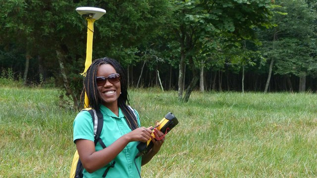 Intern holding a GPS unit and wearing a backpack GPS device