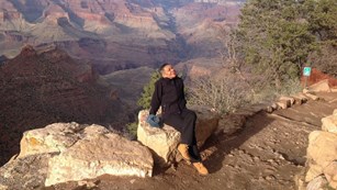 Visitor sitting on a rock next to a canyon