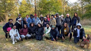 A large group of youth and a dog posing for a picture in a wooded area