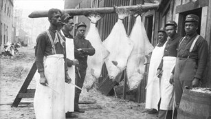 Historic black and white photo of a group of Black soldiers preparing halibut