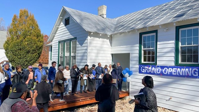 A group of about two dozen people outside an historic white building for its grand opening.
