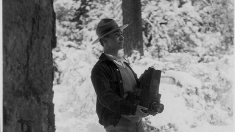 Black and white historic photo of George Wright holding a camera in the woods