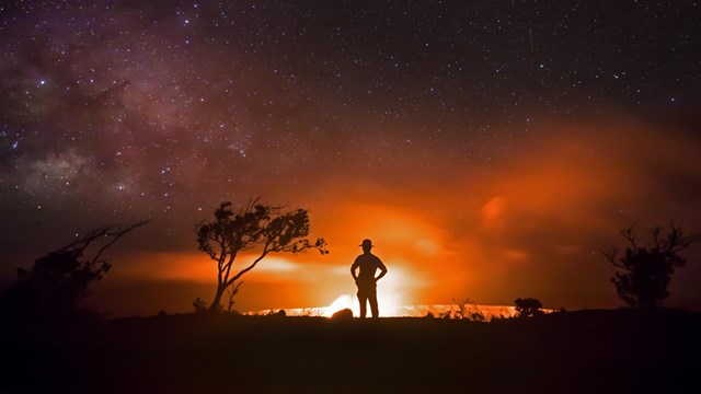 Silhouette of person against a lava eruption at night
