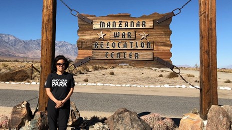 Kim Hirose Tobe standing in front of a sign for Manzanar War Relocation Center
