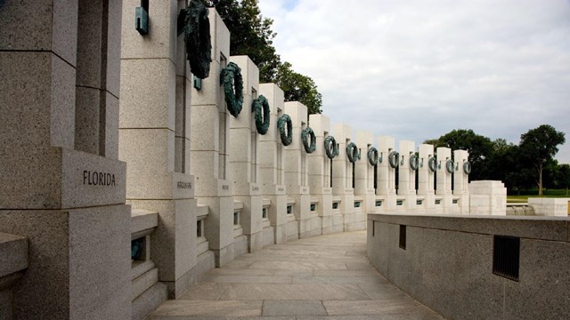 Memorial pillars in a curved line each with the name of a state and a metal wreath