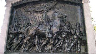 Bas-relief of a soldier on horseback riding along a line of marching soldiers