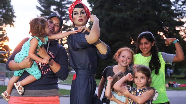 Group of kids and adult  interacting with a Rosie the Riveter statue