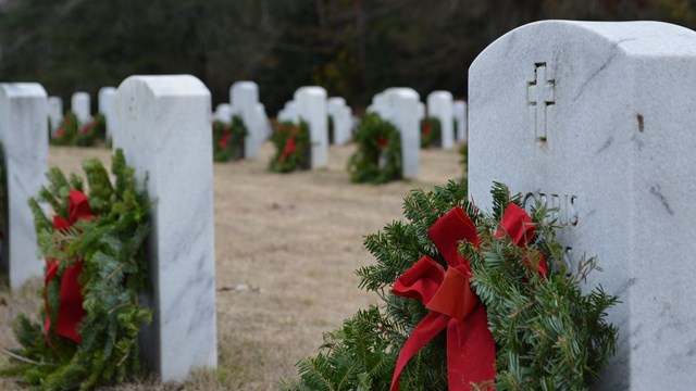 Green wreaths with red ribbons resting against headstones at a cemetery